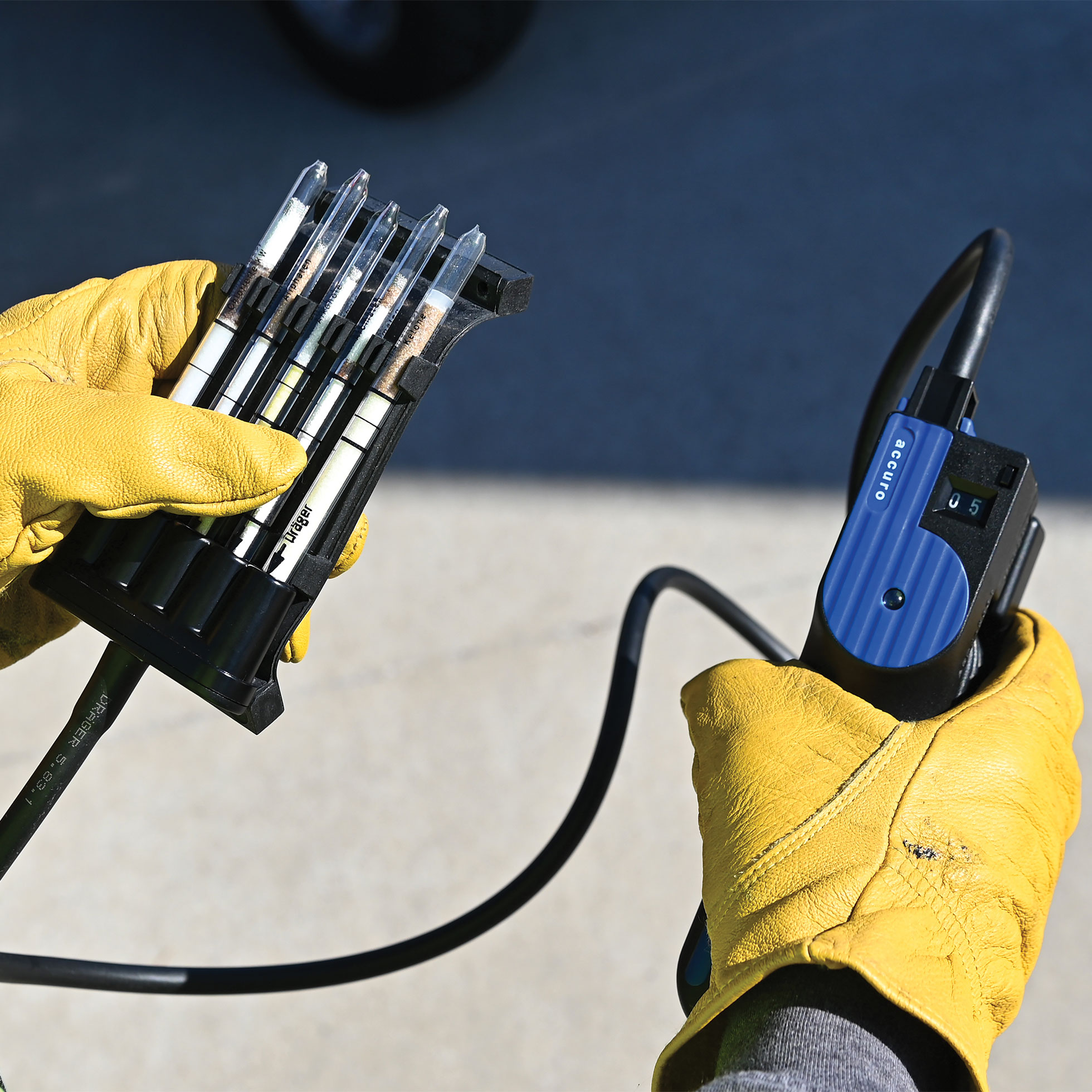 Person mit gelben Arbeitshandschuhen hält ein Messgerät und einen Verlängerungsschlauch von Dräger Accuro zur Gasmesstechnik